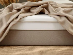 Boxspring matras met zichtbare doorzakking in het midden, antraciet hoofdbord en beige dekbed in slaapkamer