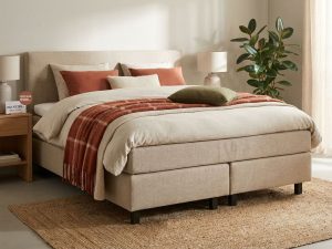Complete boxspring bed met beige gestoffeerd frame, terracotta plaid en sierkussens op jute vloerkleed met kortingsbon