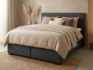 Antraciet boxspring met beige dekbed, sierkussens en plaid in rustieke slaapkamer met jute vloerkleed en pampasgras
