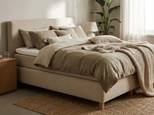 Complete boxspring bed met beige gestoffeerd frame in slaapkamer, dekbed en sierkussens, jute vloerkleed, zachte verlichting