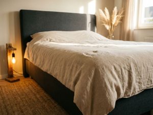 Boxspring bed met slijtage op beige dekbed, antraciet hoofdbord, jute vloerkleed en warme verlichting in slaapkamer