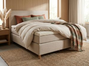Beige boxspring bed met dekbed, terracotta kussens en natuurlijke ochtendbelichting in warme slaapkamer