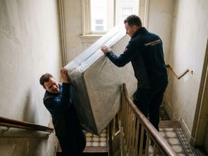 Twee bezorgers tillen ingepakte boxspring voorzichtig Nederlandse trap op, professionele meubellevering service