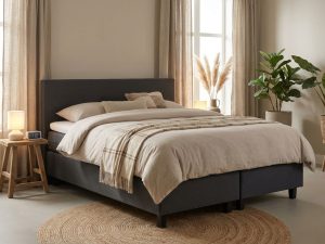 Complete boxspring bed met antraciet gestoffeerd frame in warme slaapkamer met beige plaid, kussens en zachte verlichting