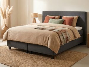 Donkergrijze boxspring met stevig hoofdbord en beige dekbed in warme slaapkamer met terracotta kussens