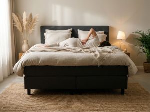 Persoon met rugpijn ligt op antraciet boxspring bed in moderne slaapkamer met natuurlijke decoratie