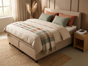 Beige boxspring bed met terracotta kussens in Nederlandse slaapkamer, rekenmachine op nachtkastje, natuurlijke decoratie