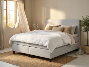 Lichtgrijze boxspring met wit dekbed in zonnige slaapkamer met ventilator en open raam voor zomercomfort