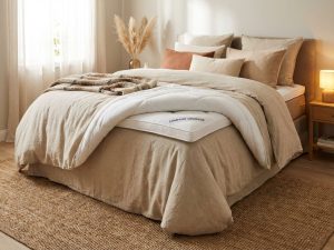 Boxspring bed met witte topper half opgevouwen aan voeteneinde in warme beige slaapkamer met natuurlijke belichting