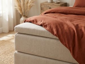 Beige boxspring topper met terracotta dekbed in rustgevende slaapkamer met natuurlijke ochtendbelichting