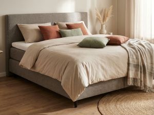 Boxspring tweepersoonsbed met grijs hoofdbord en beige beddengoed in moderne slaapkamer met natuurlijk licht