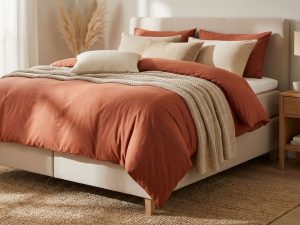 Luxe terracotta dekbed op beige boxspring met sierkussens en gebreide plaid in stijlvolle slaapkamer setting
