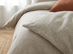 Luxe beddengoed close-up toont fijne weefstructuur en draadkwaliteit in beige en grijstinten met terracotta kussens