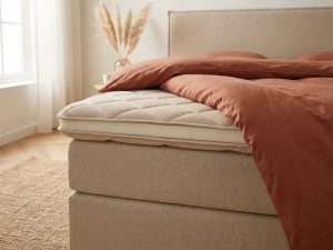 Matrastopper voor buikslapers op bed met terracotta dekbed en natuurlijke verlichting in beige slaapkamer
