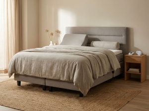 Orthopedische boxspring met grijs hoofdbord in rustgevende slaapkamer met therapeutische accessoires en natuurlijke belichting