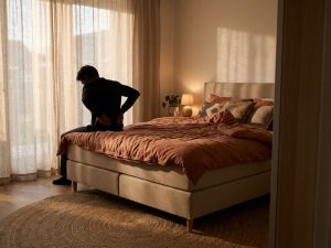 Persoon met rugpijn zittend op boxspring bed bij dageraad in natuurlijk gestyleerde slaapkamer